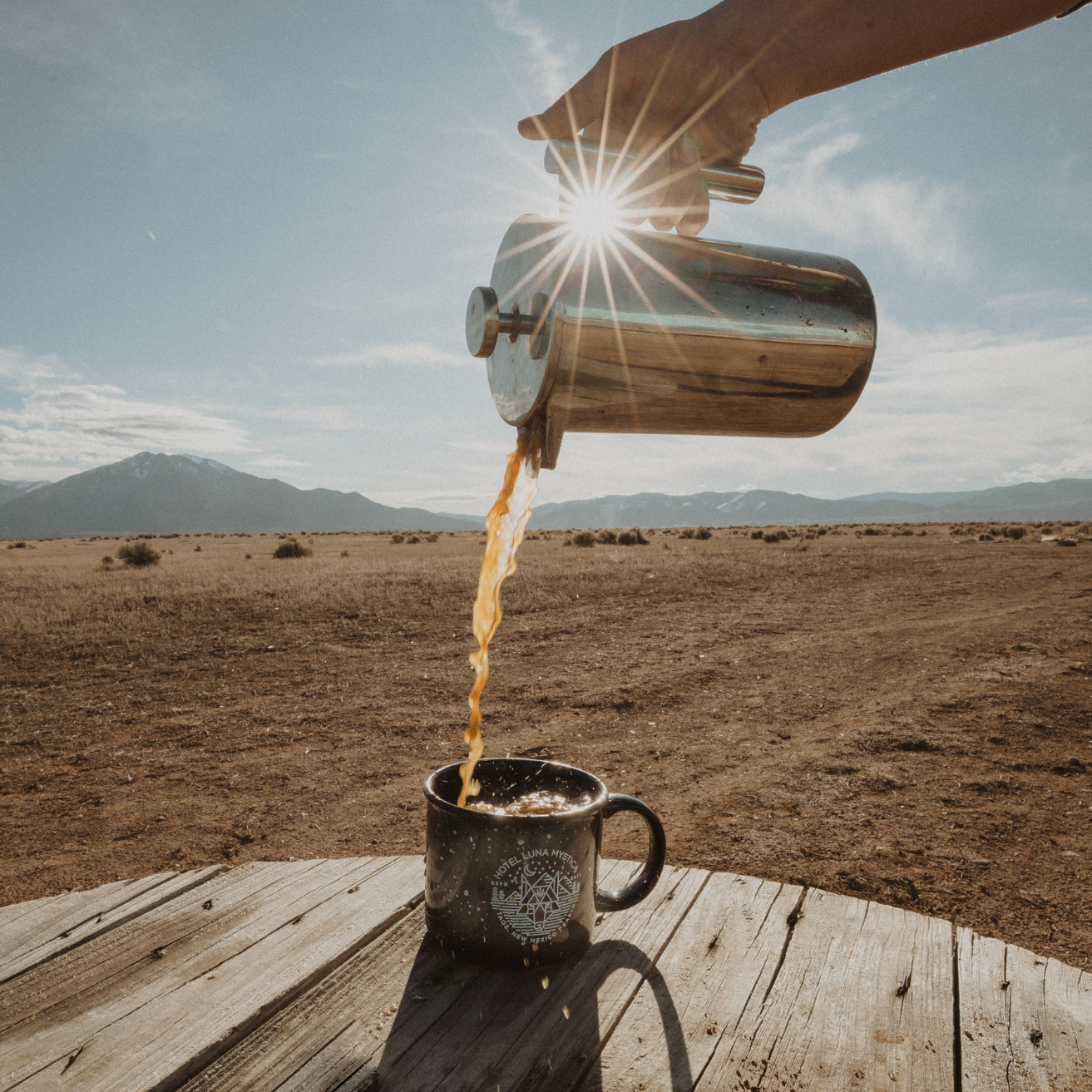 Person pouring coffee from a French press into a mug with a scenic desert background