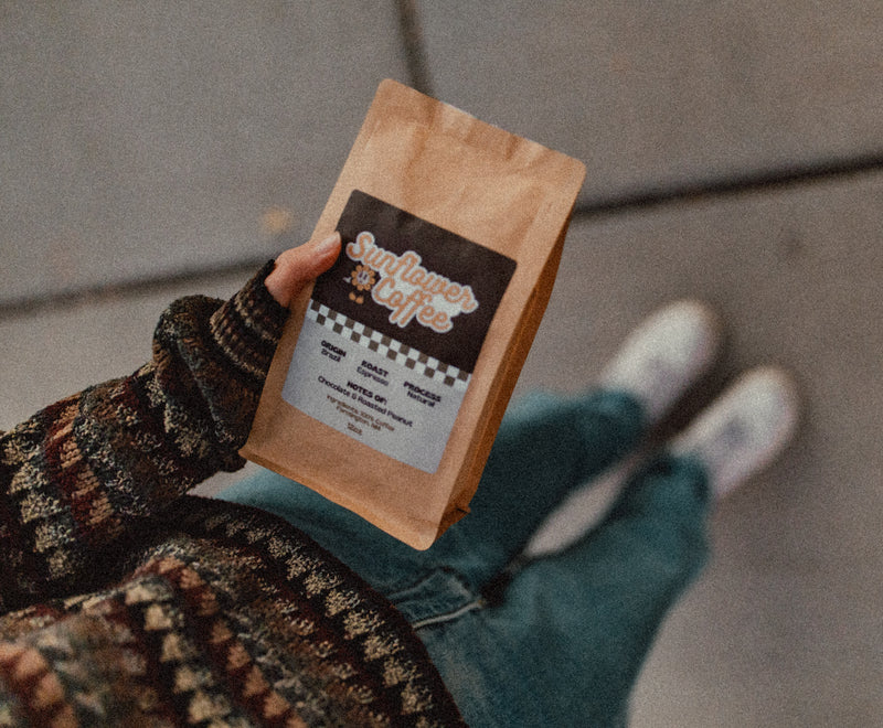 Person holding a brown paper bag with 'Sunflower Coffee' label on a blurred background