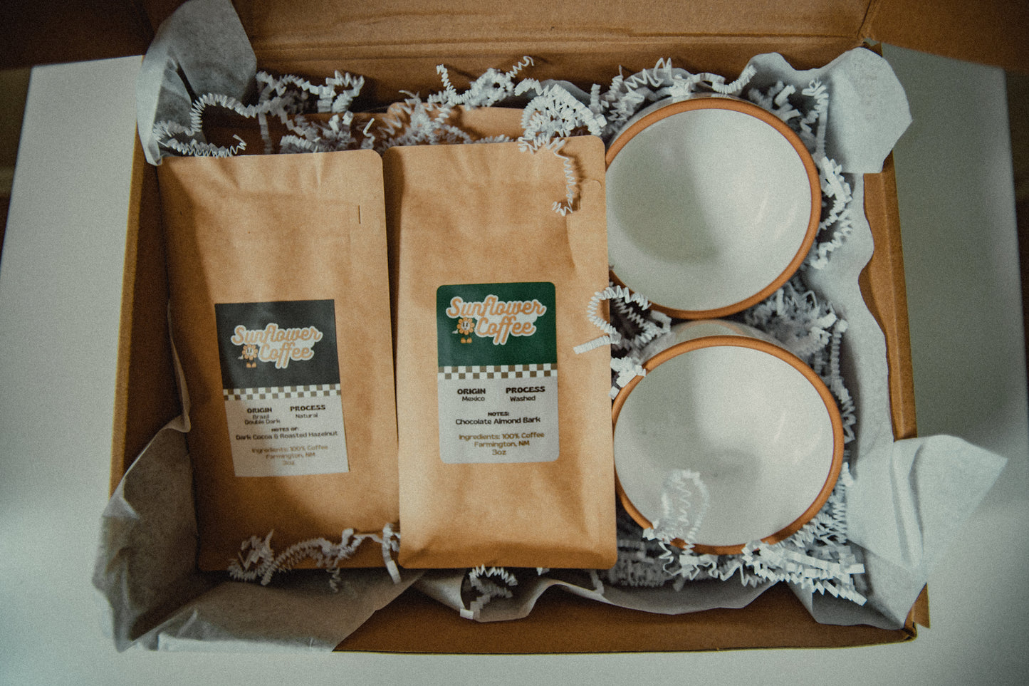 Two coffee bags and two ceramic bowls in a box with shredded paper