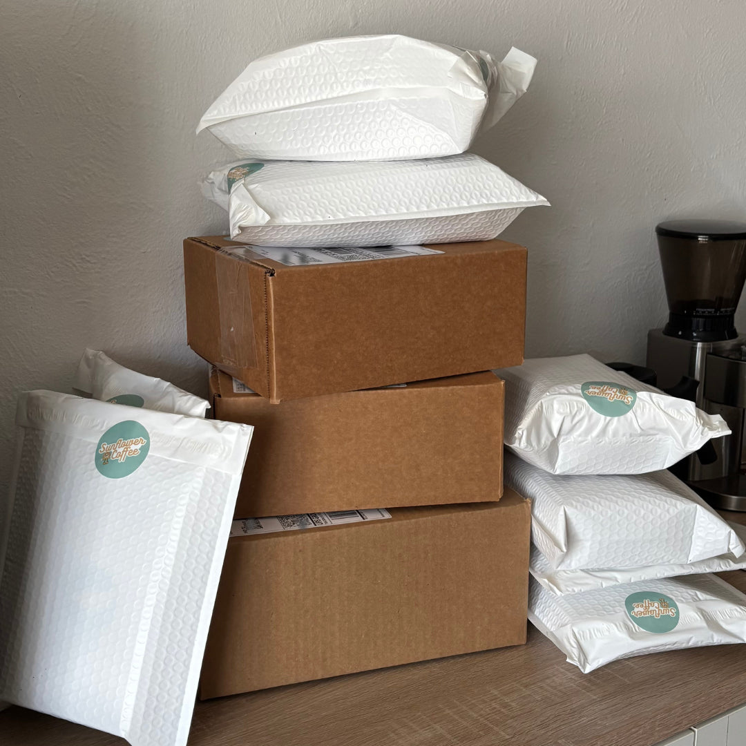 Stack of brown cardboard boxes and white bubble mailers on a wooden surface.